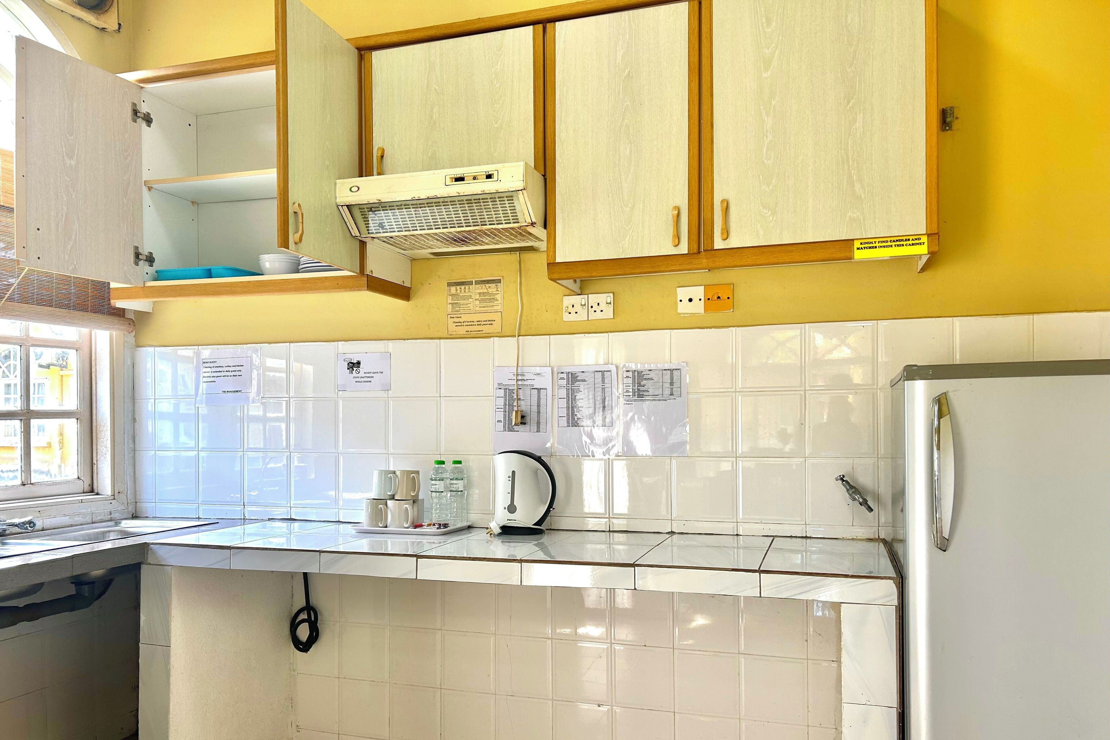 Una cocina con armarios blancos, un refrigerador blanco, un hervidor y una ventana con vista a edificios.