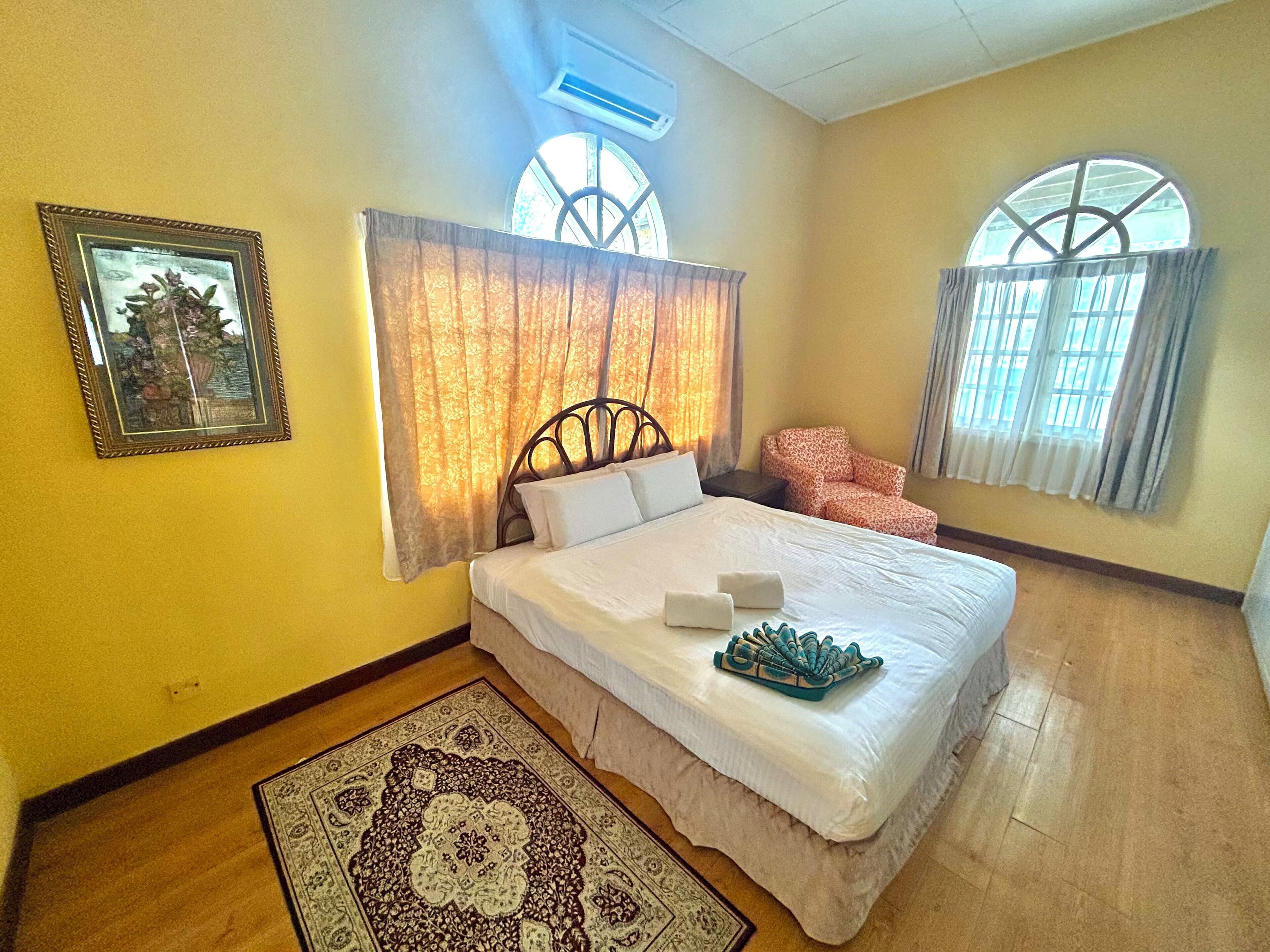 Un dormitorio con una cama, una silla, un tapete y dos ventanas.
