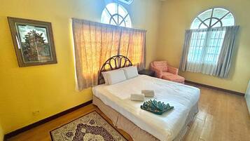 A bedroom with a bed, a chair, a rug, and two windows.