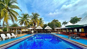 A swimming pool with lounge chairs and umbrellas, surrounded by palm trees and a building with a tiled roof. - RUMBIA RESORT VILLA Paka Terengganu  (Dungun)