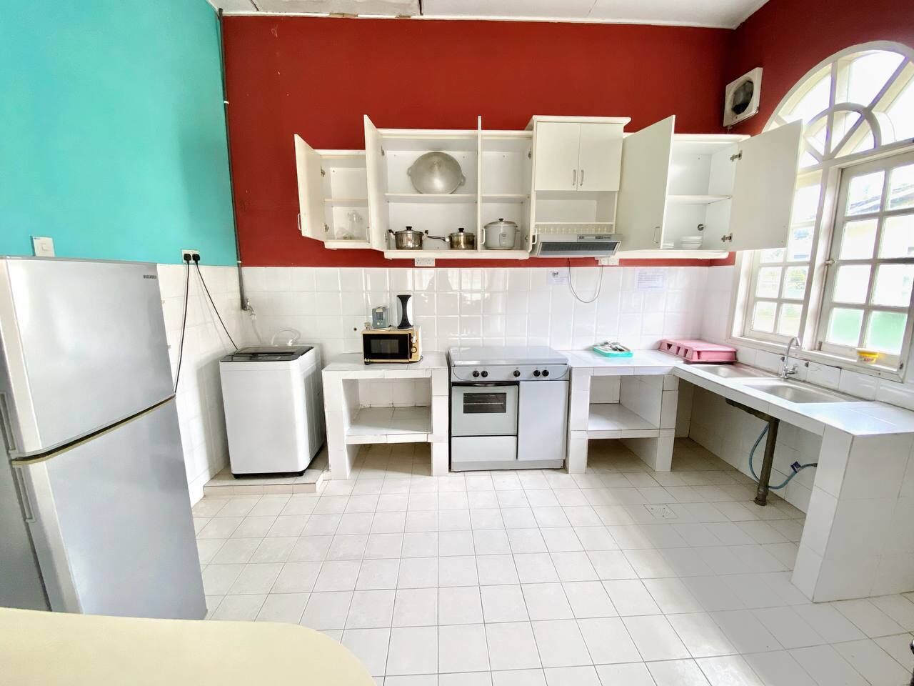 Una cocina compacta con armarios blancos, un microondas, una estufa y un refrigerador.
