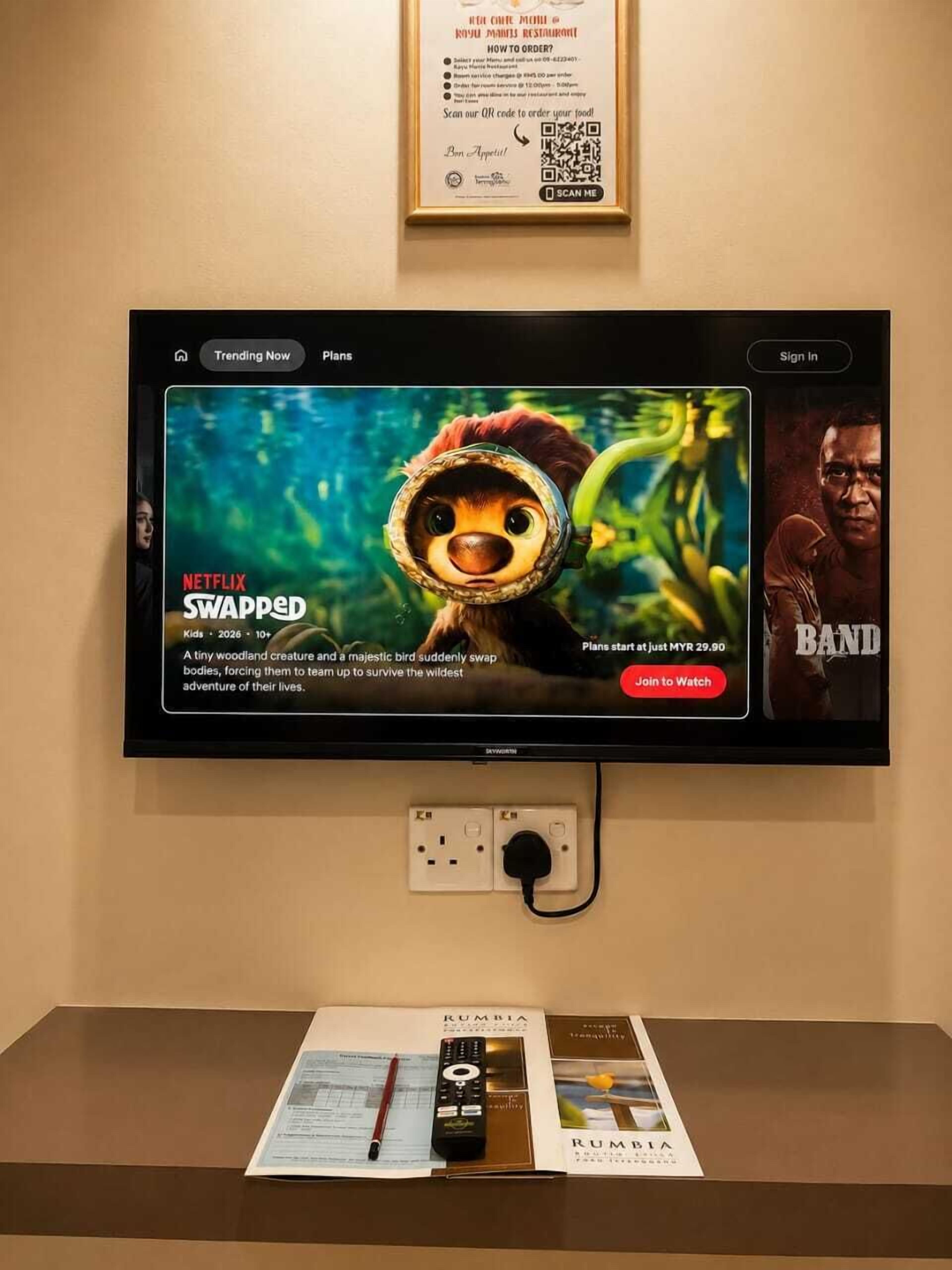 A television displaying a movie poster for 'Swapped' on Netflix, a sign with QR code, and a remote control on a table.