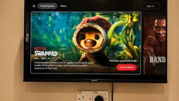 A television displaying a movie poster for 'Swapped' on Netflix, a sign with QR code, and a remote control on a table.