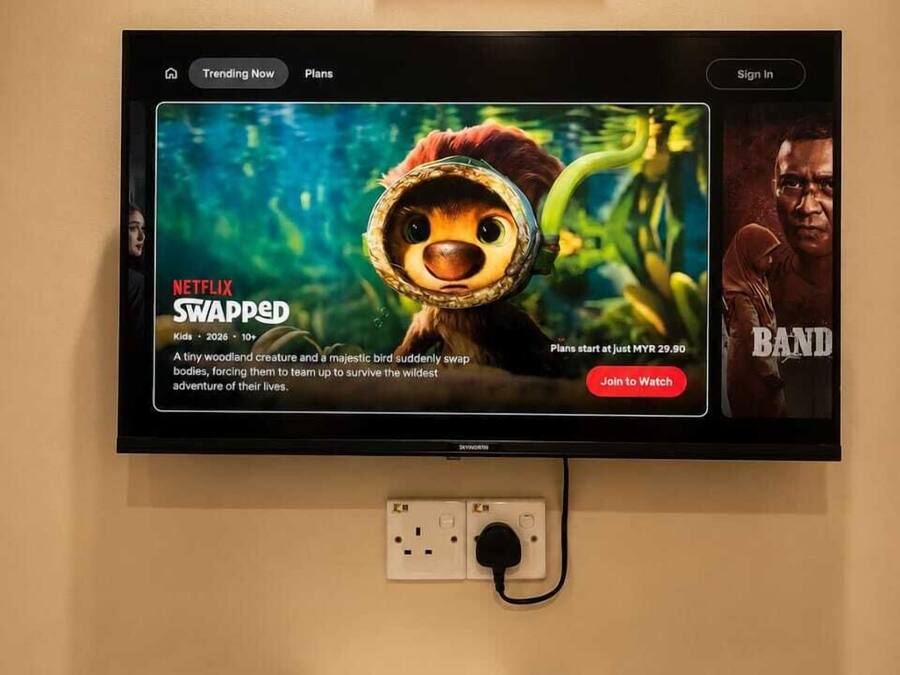 A television displaying a movie poster for 'Swapped' on Netflix, a sign with QR code, and a remote control on a table.