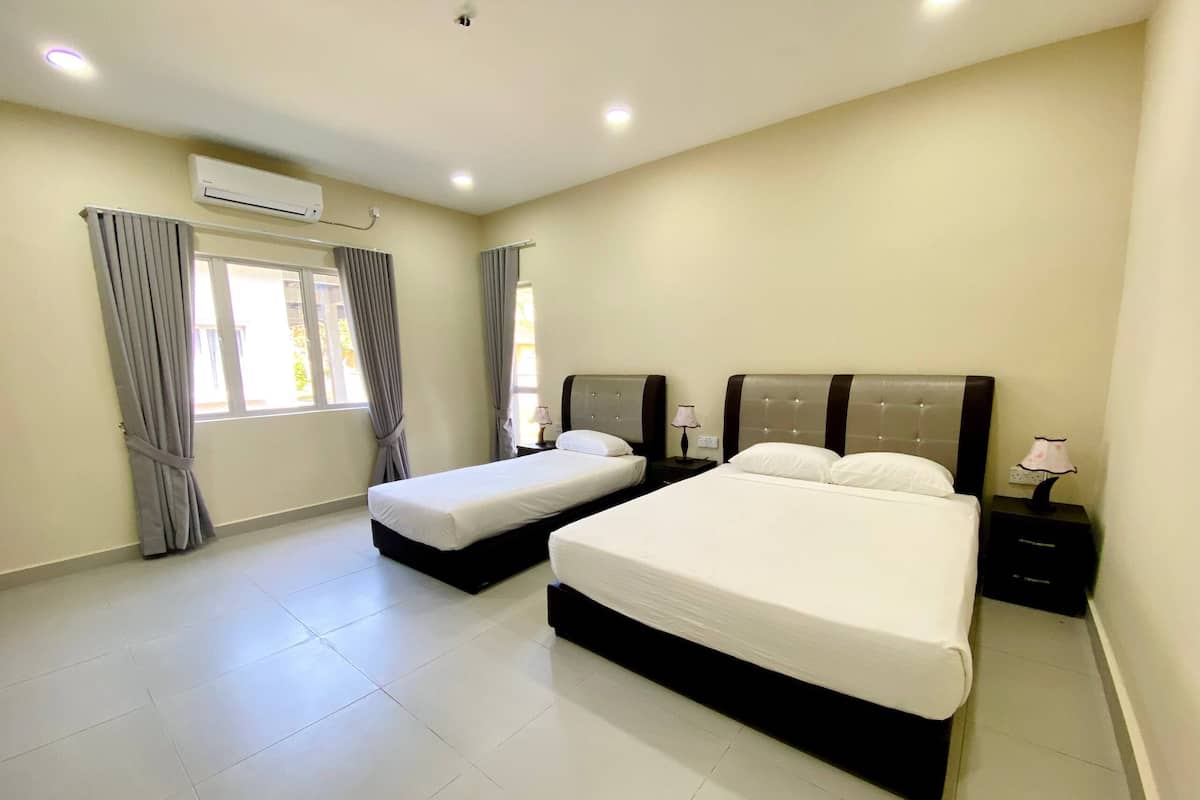 A hotel room with two beds, a window with curtains, an air conditioning unit, and a nightstand with a lamp.