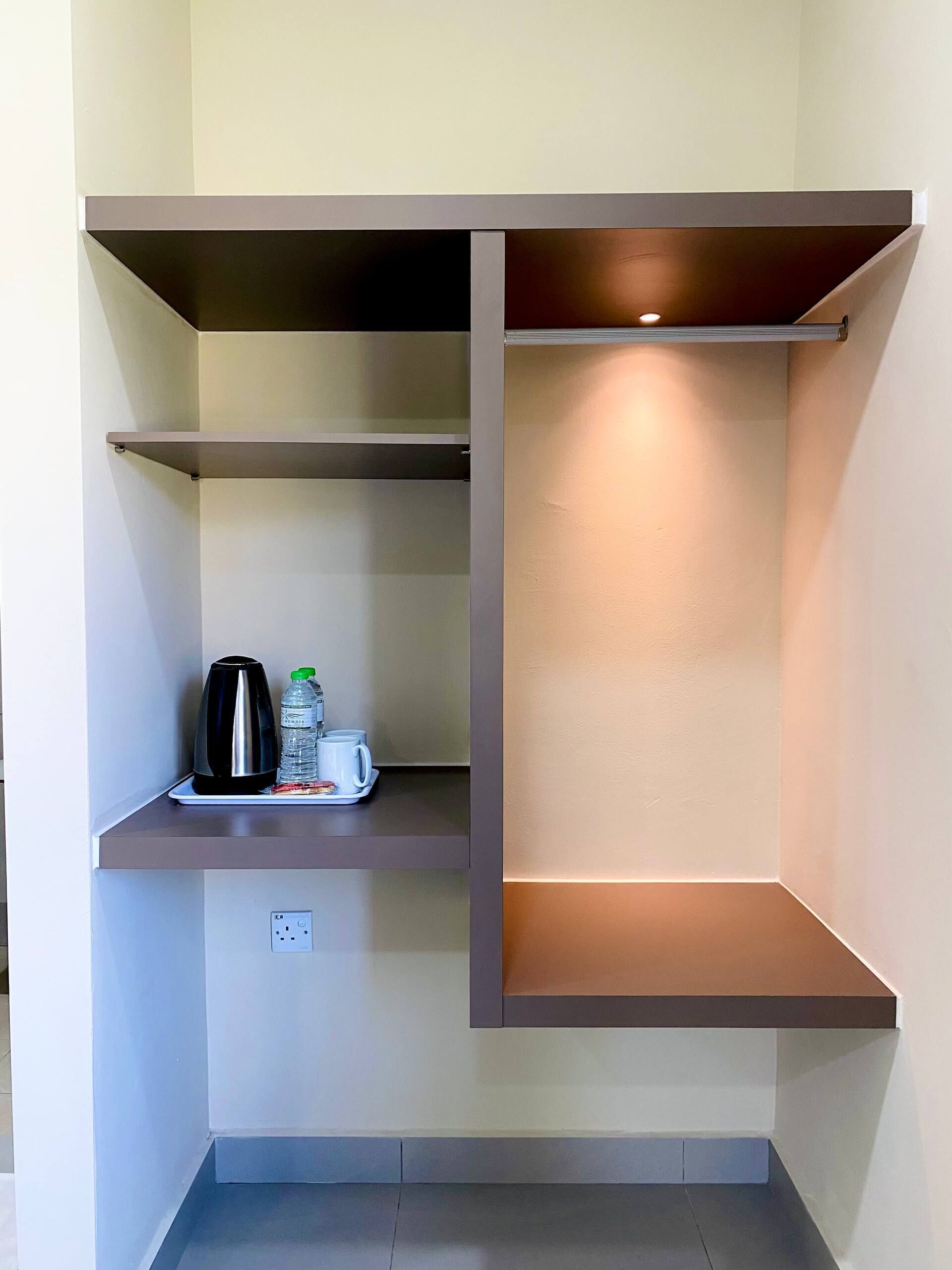 A kitchenette with a coffee maker, water bottles, and a cup on a shelf.