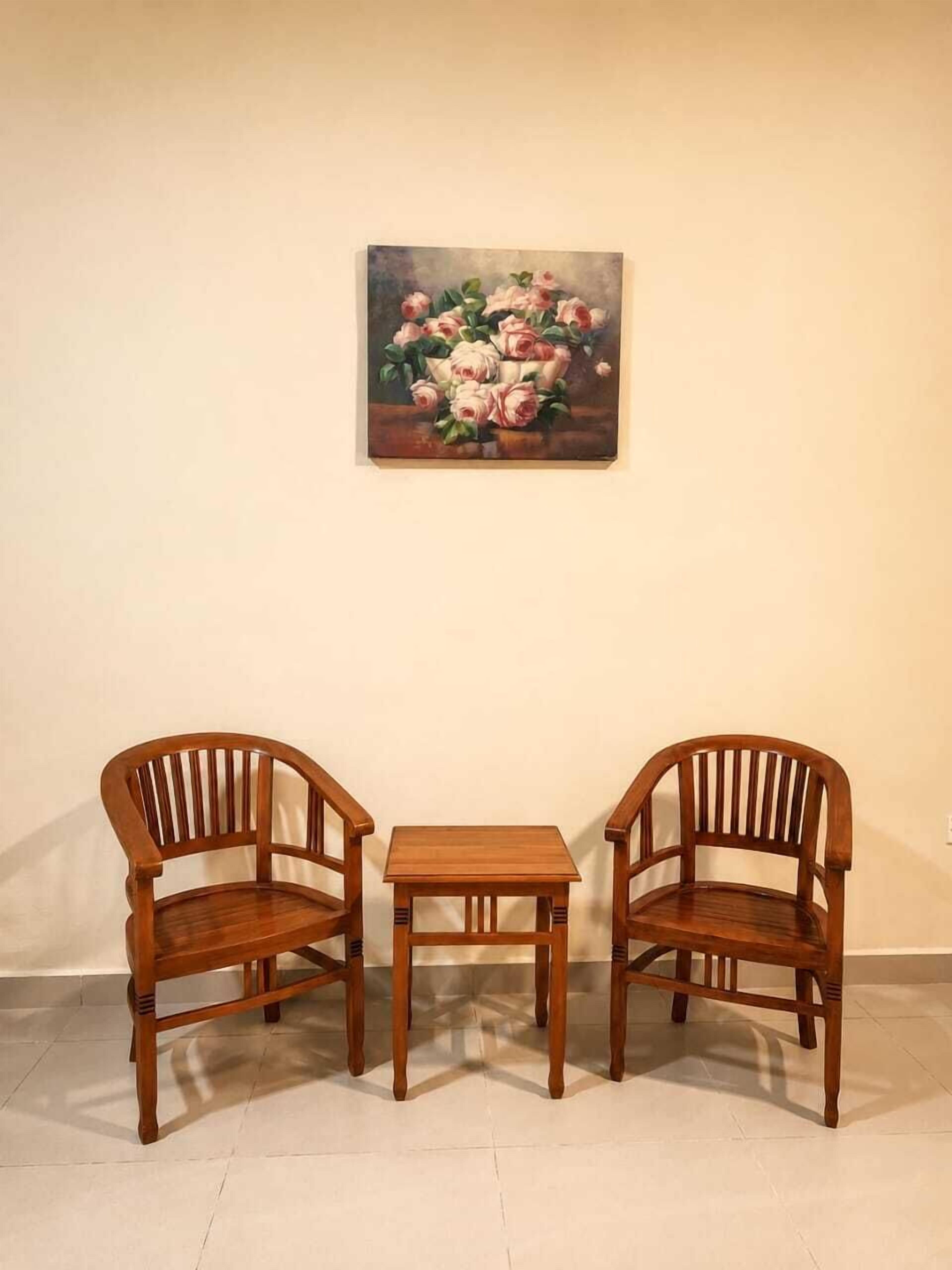A room with a painting of flowers on the wall, two wooden chairs, and a small table.