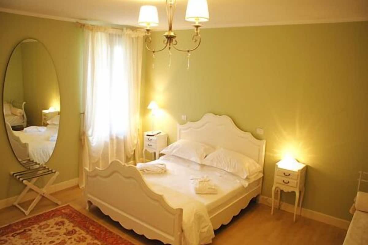 Una cama bien hecha con sábanas blancas, un espejo grande y dos lámparas de noche.