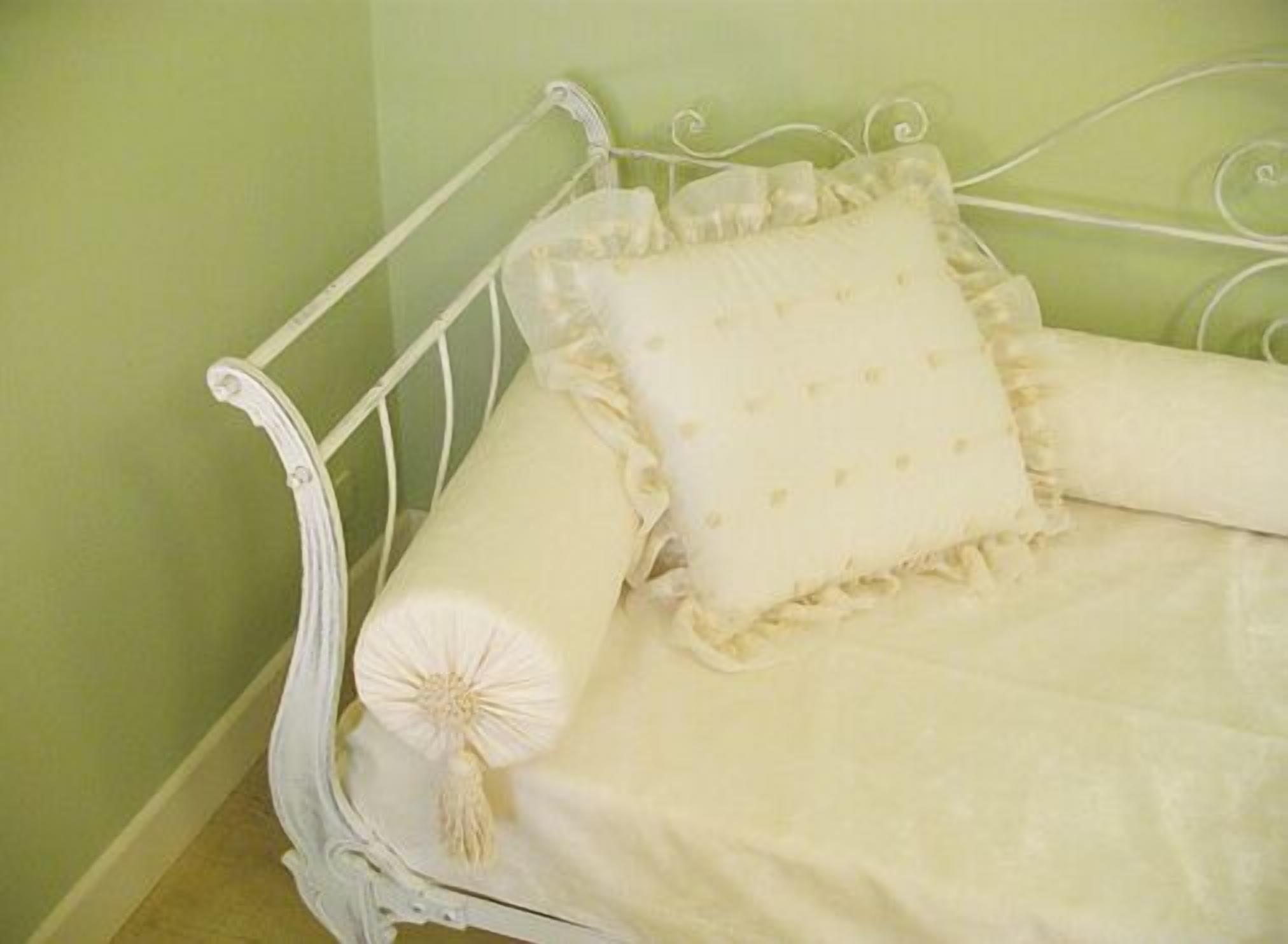 Een wit metalen bed met een gefranseerd kussen en een opgerolde deken.
