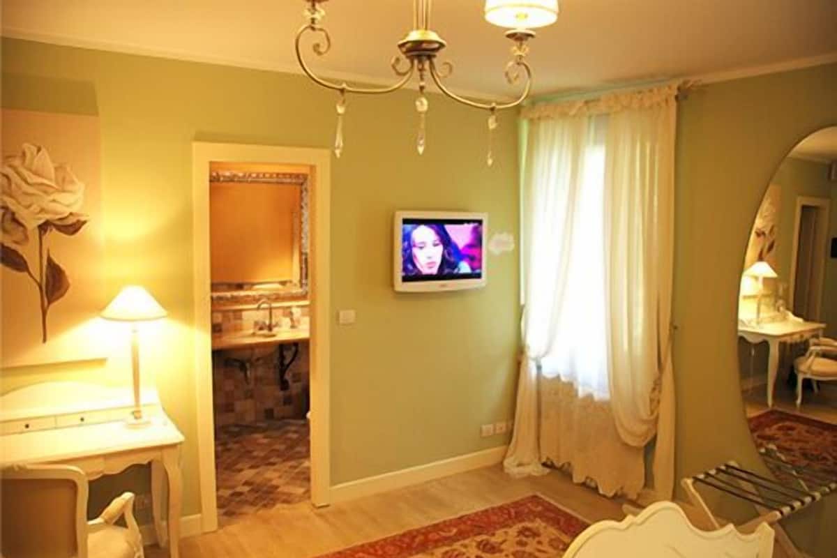 Un dormitorio con cama, televisor, espejo, tocador con lavabo y candelabro.