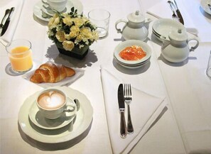A breakfast setting with a croissant, coffee, orange juice, and a flower arrangement on a table. - Villa Chiopris (Chiopris-Viscone)
