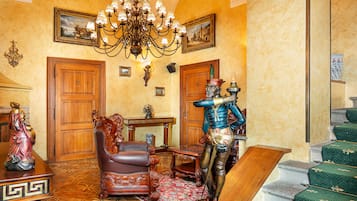 A stately room with a chandelier, wooden doors, a statue, a chair, and a staircase.