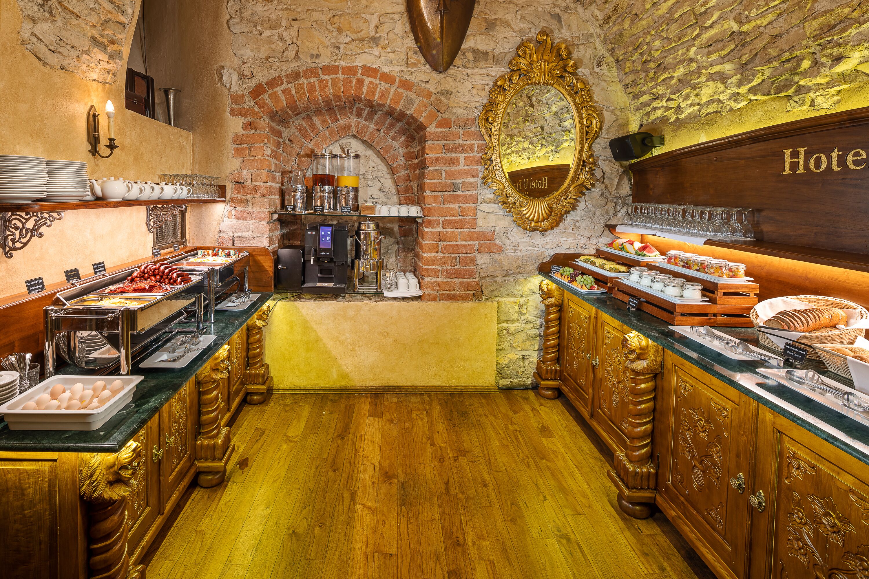 A hotel breakfast area with a brick wall, wooden cabinets, and a buffet with various food items.