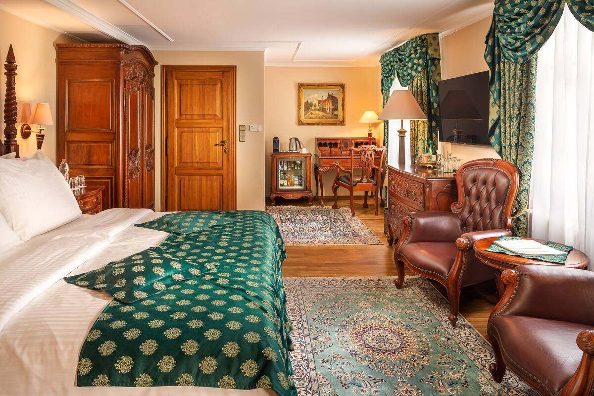 Une chambre d’hôtel avec un grand lit, deux fauteuils, un bureau, une télévision et un tableau au mur.