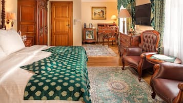 A hotel room with a large bed, a sitting area with a chair and a table, a desk with a computer, and a television.