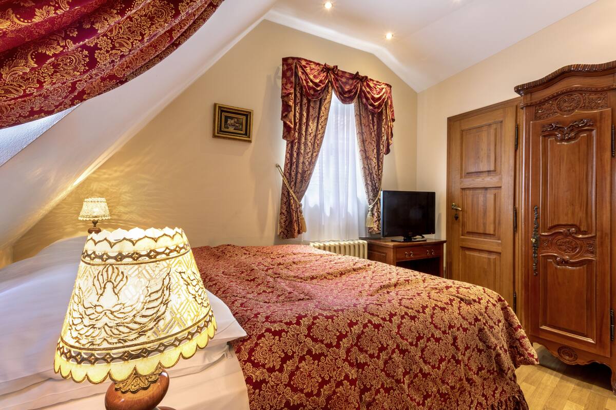 Une chambre à coucher avec un lit, une lampe, une télévision et une armoire.