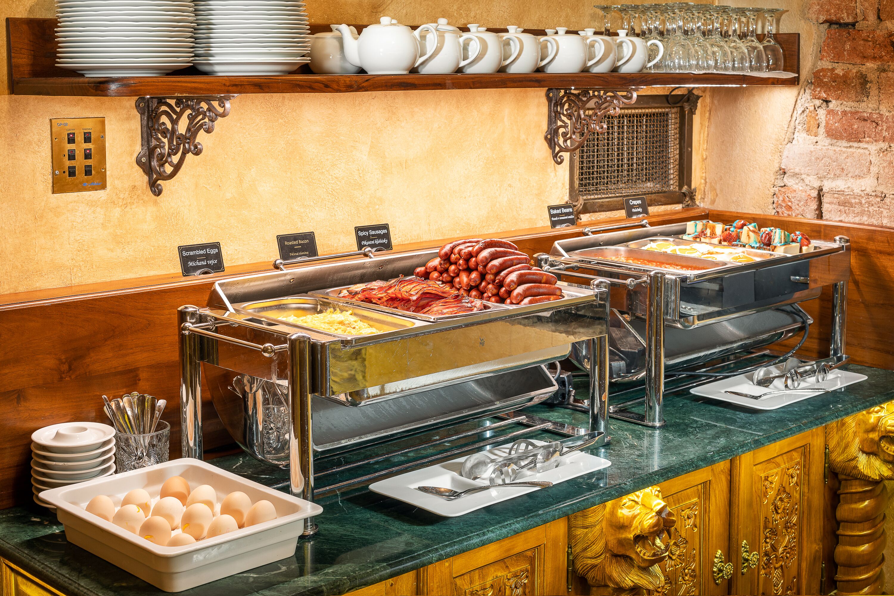 A buffet with various food options, including scrambled eggs, sausages, and a tray of eggs.