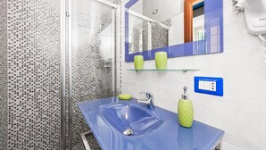 A bathroom with a glass shower enclosure, a blue sink, and a mirror with a blue frame. - La Casa Di Elena (Rome)