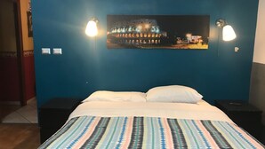 A hotel room with a bed, two bedside tables, a nightstand, a wall-mounted picture of a building, and two wall-mounted lamps. - La Casa Di Elena (Rome)