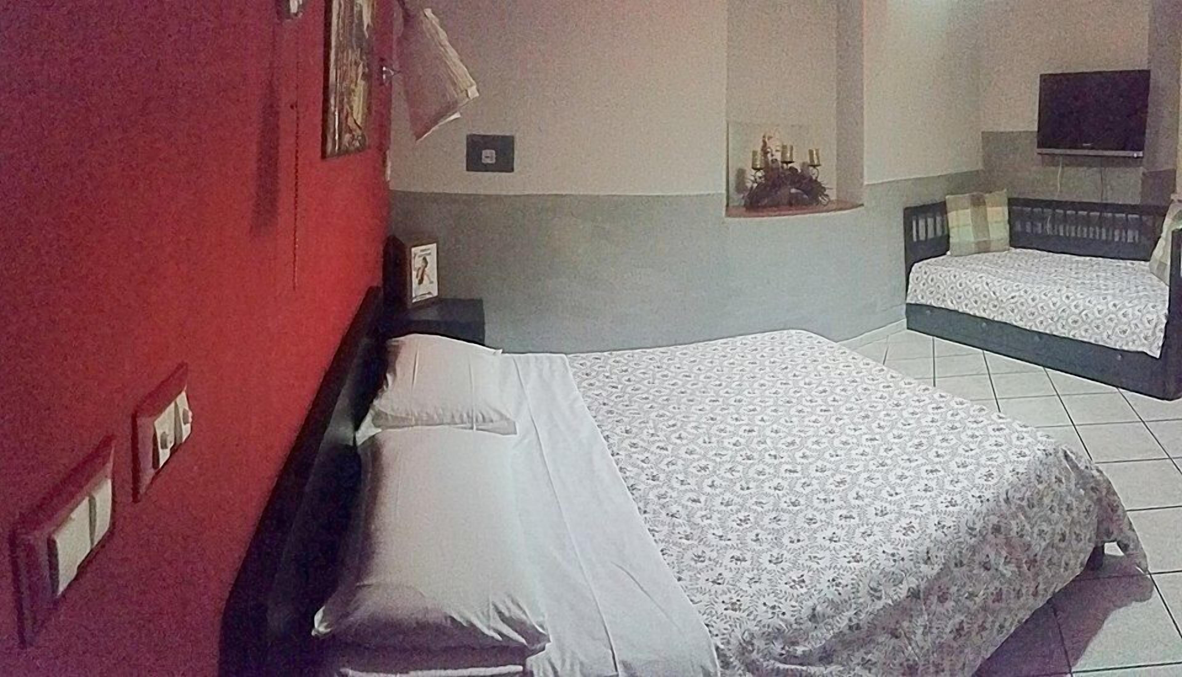A bedroom with a large bed, a smaller bed, a television, and a wall-mounted shelf with decorative items.