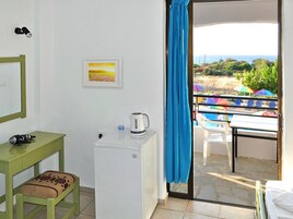 Una habitación con un refrigerador blanco pequeño, una mesa verde con una silla, un cuadro en la pared y vistas a un área de piscina con sombrillas.