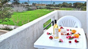 A balcony with a table set for two, featuring a bottle of wine, two glasses, and scattered flowers. - Greta Beach (Hersonissos)