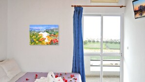A bedroom with a bed, a painting, and a view through a glass door. - Greta Beach (Hersonissos)