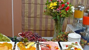 A buffet table with various food items, including fruits, cheeses, and meats, and a flower vase in the background. - Greta Beach (Hersonissos)