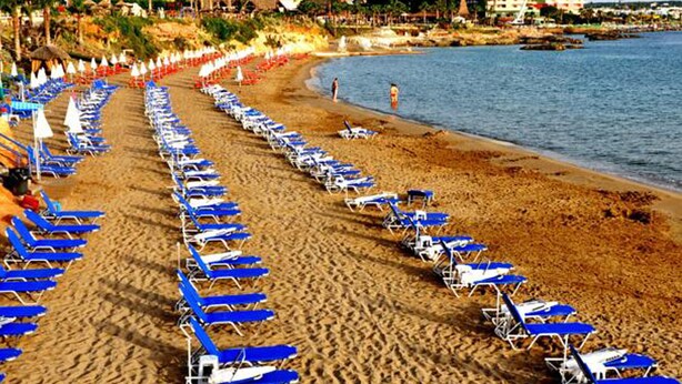 A beach with rows of blue and white sun loungers facing the ocean. - Greta Beach (Hersonissos)
