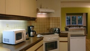 Cocina compacta con microondas, estufa y tostadora. Se ve un refrigerador pequeño al fondo.