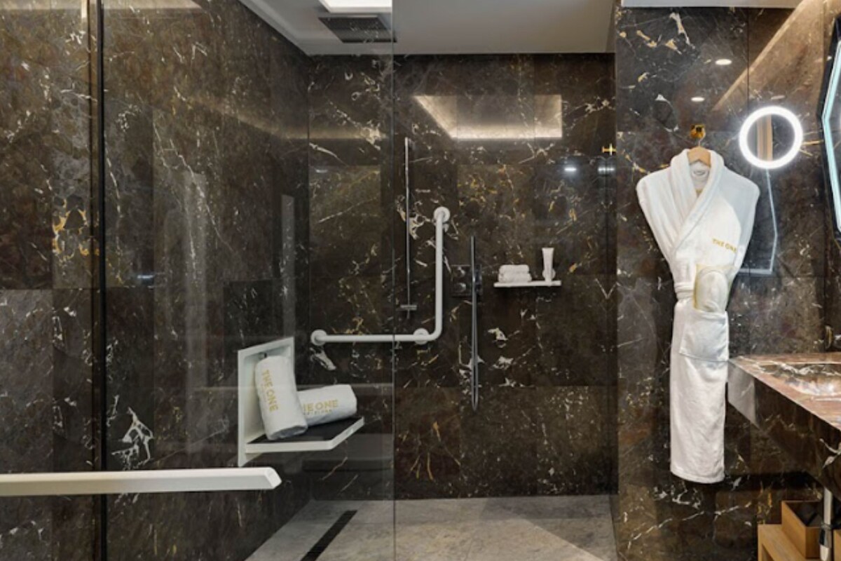 A modern bathroom with a glass-enclosed shower, a vanity with a mirror, and a robe hanging on a rack.