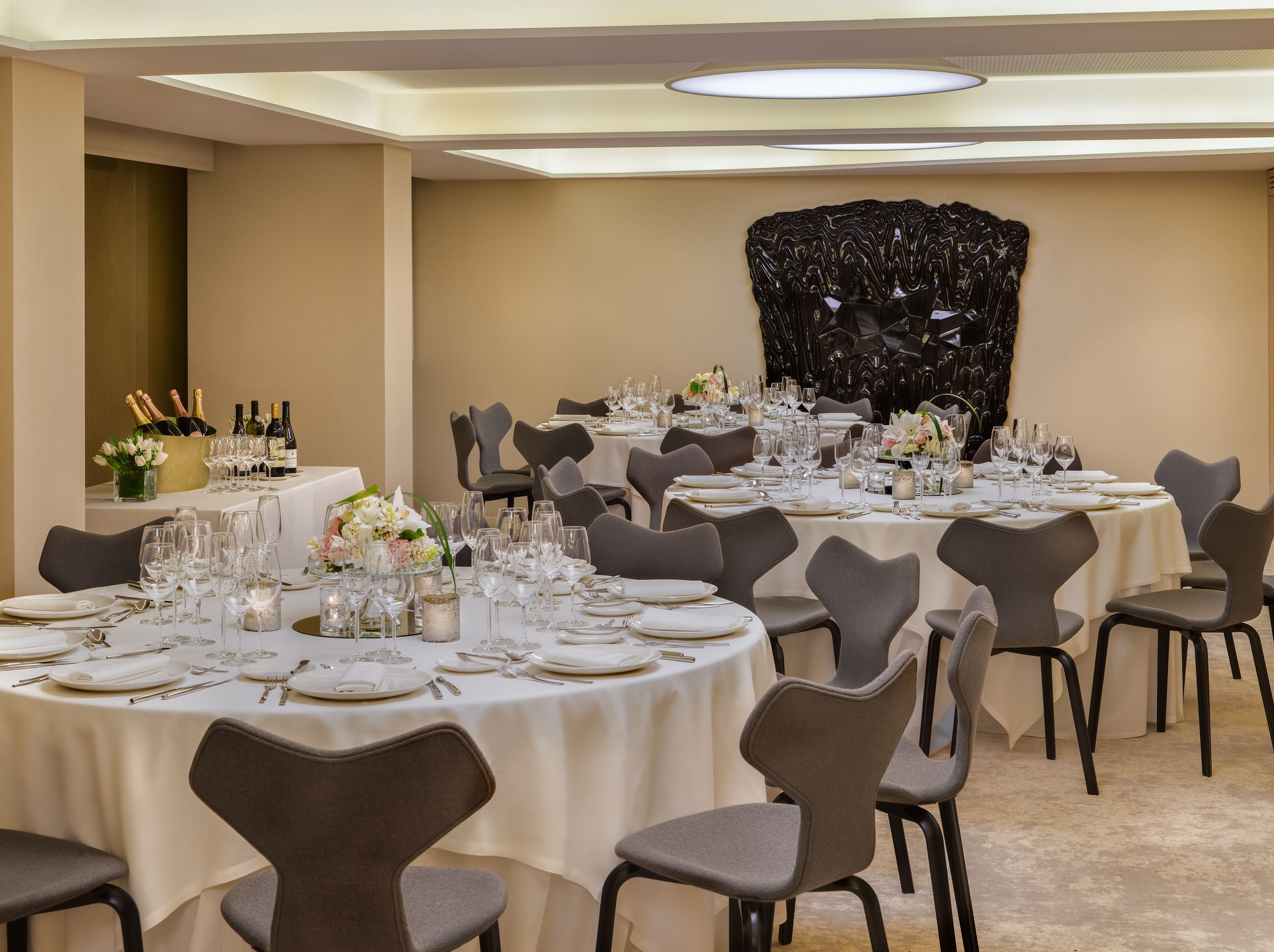 Un salón de banquetes con mesas redondas dispuestas para un evento formal, con manteles blancos, cubiertos y cristalería.