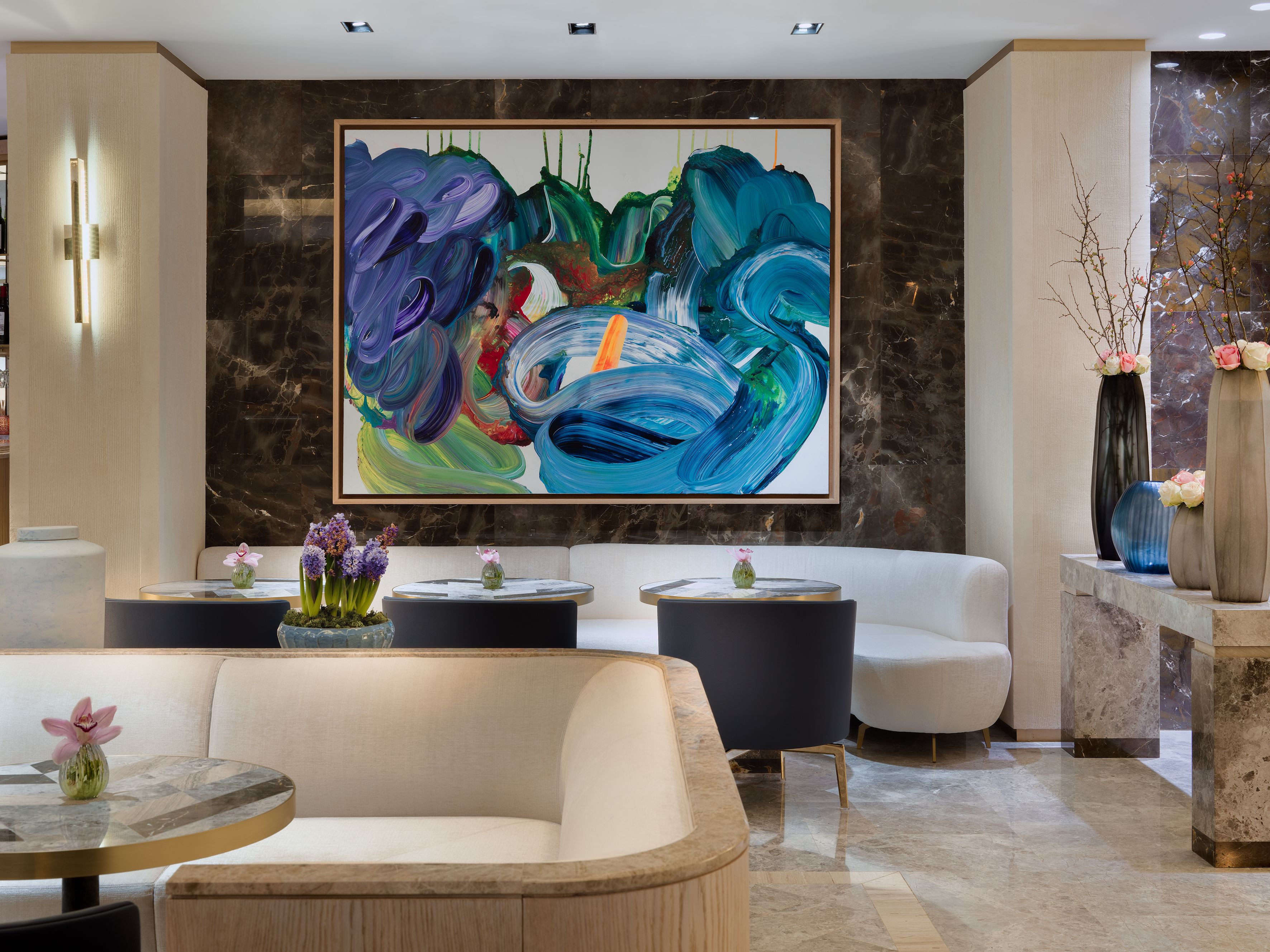 A modern lobby with a large abstract painting, comfortable seating, and decorative vases.