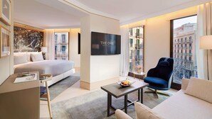 A modern hotel room with a bed, a sofa, a TV, and a view of the city. - The One Barcelona GL (Barcelona)