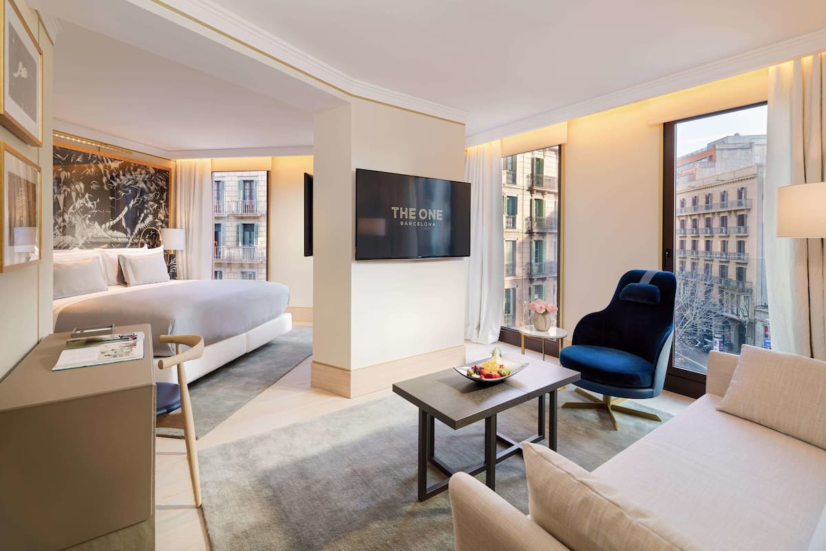 A modern hotel room with a bed, a sofa, a TV, and a view of the city.