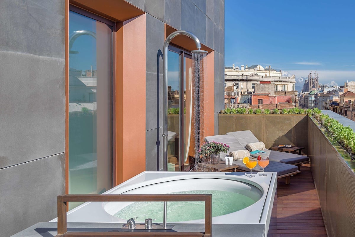 A rooftop terrace with a hot tub, seating area, and a view of the cityscape.