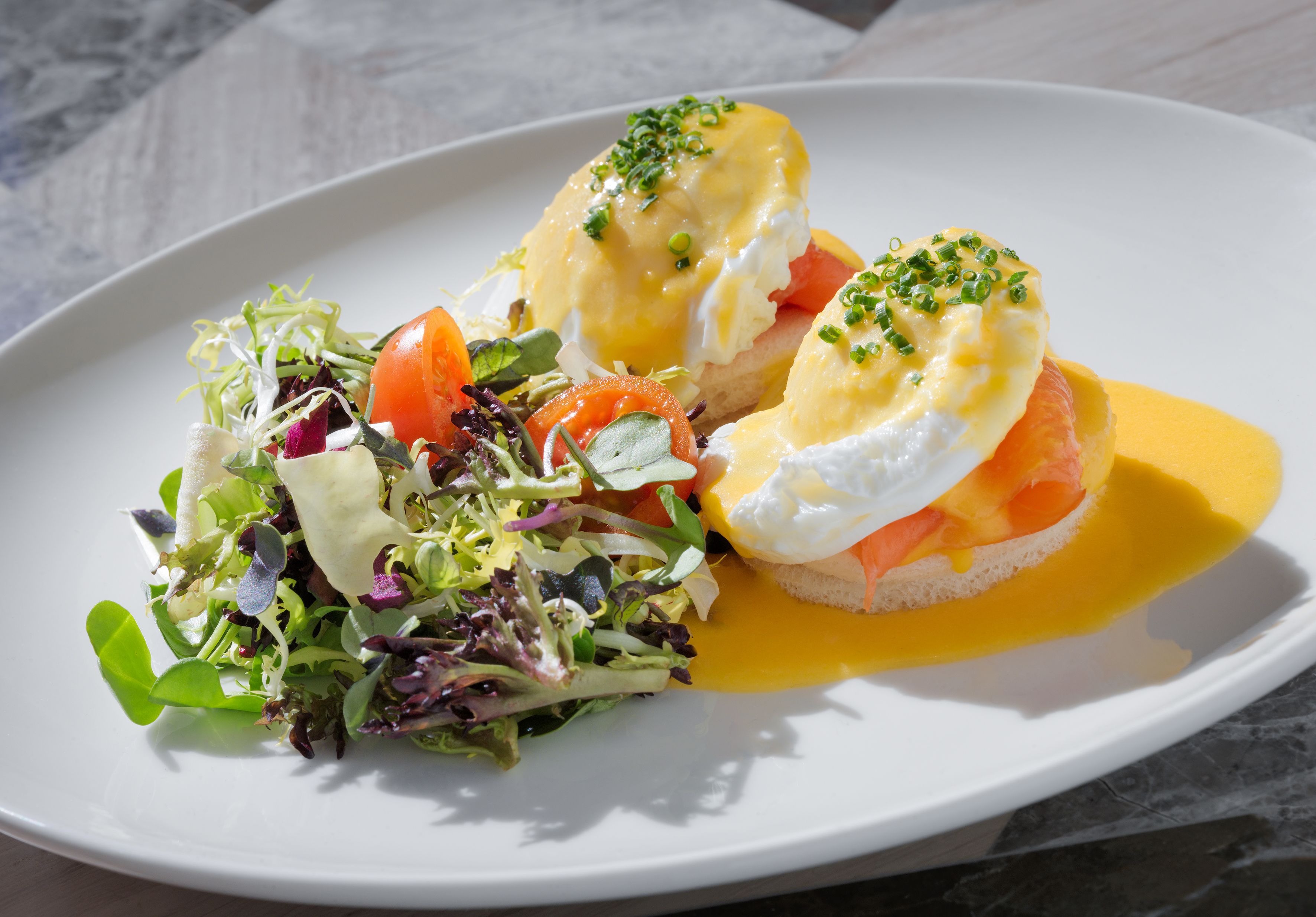 A plate with eggs benedict, a side salad, and a slice of toast.