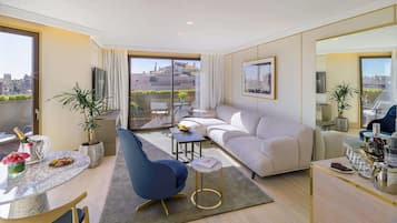 A modern living room with a sofa, a blue chair, a small table with a bottle and glasses, and a balcony with a view of buildings.