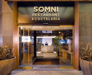The entrance to SOMNI RESTAURANT & COCTELERIA with a modern design, glass doors, and potted plants. - The One Barcelona GL (Barcelona)