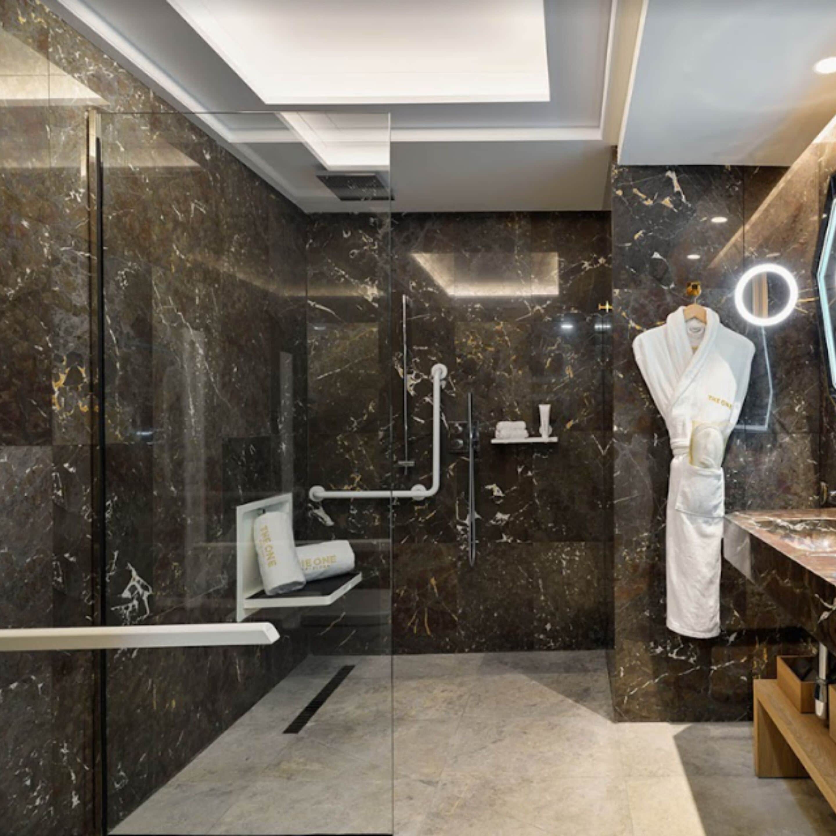 A modern bathroom with a glass-enclosed shower, a vanity with a mirror, and a robe hanging on a rack.