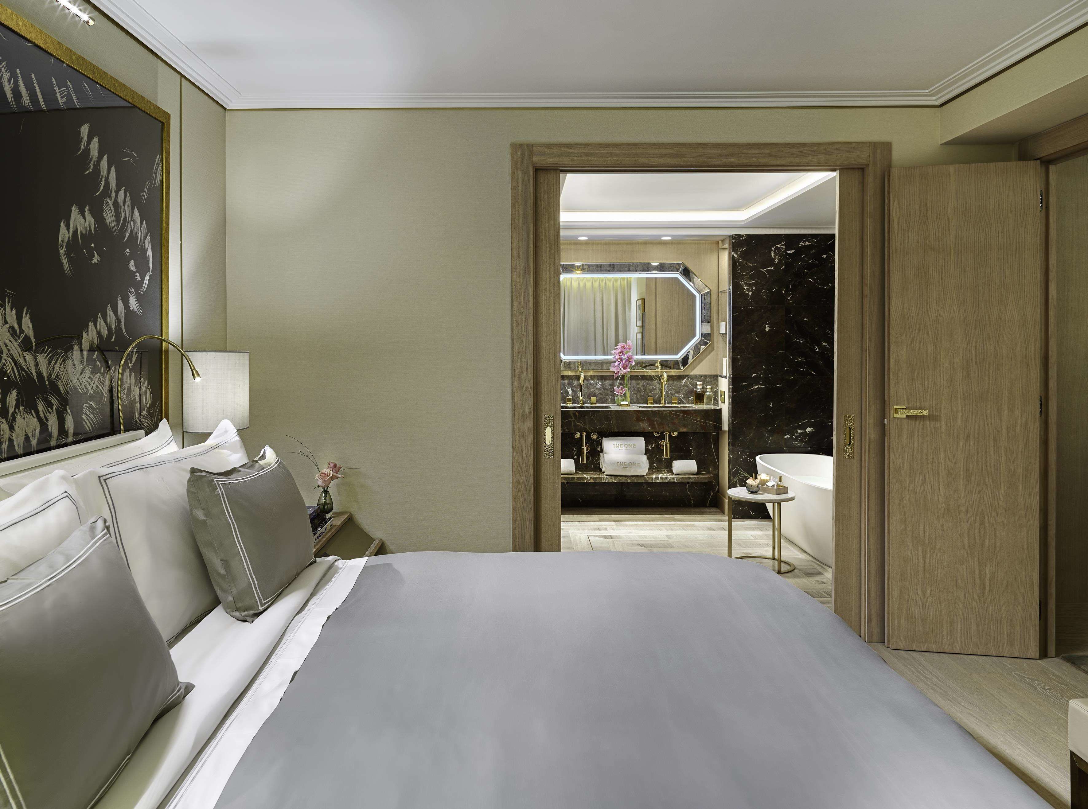 Una habitación de hotel con una cama grande, una mesita de noche, un tocador, un espejo y un baño con lavamanos y bañera.