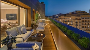 A modern balcony with a sofa, chairs, and a table, overlooking a cityscape at dusk. - The One Barcelona GL (Barcelona)