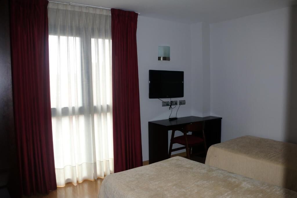 Ein Hotelzimmer mit Bett, Schreibtisch, Fernseher und einem Fenster mit roten Vorhängen.