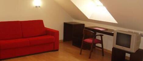 Una habitación pequeña y funcional con un sofá rojo, un escritorio, una silla y un televisor.