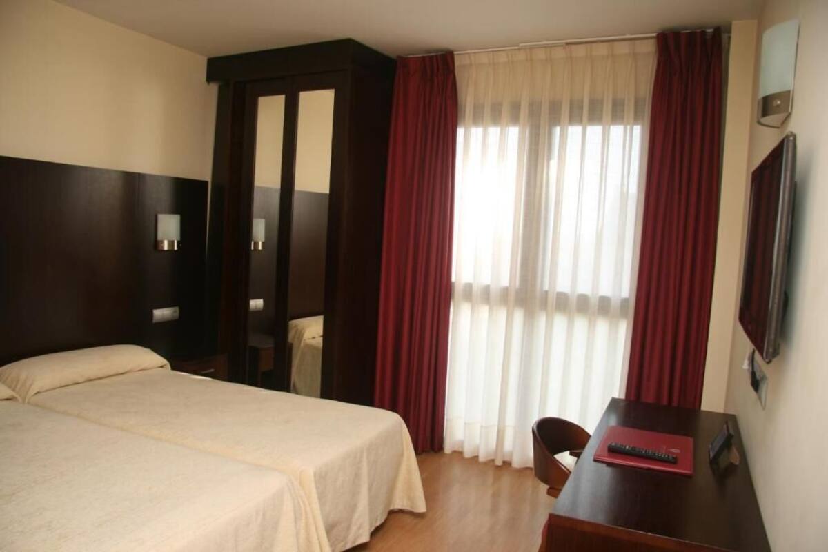 A hotel room with two beds, a desk, and a TV.