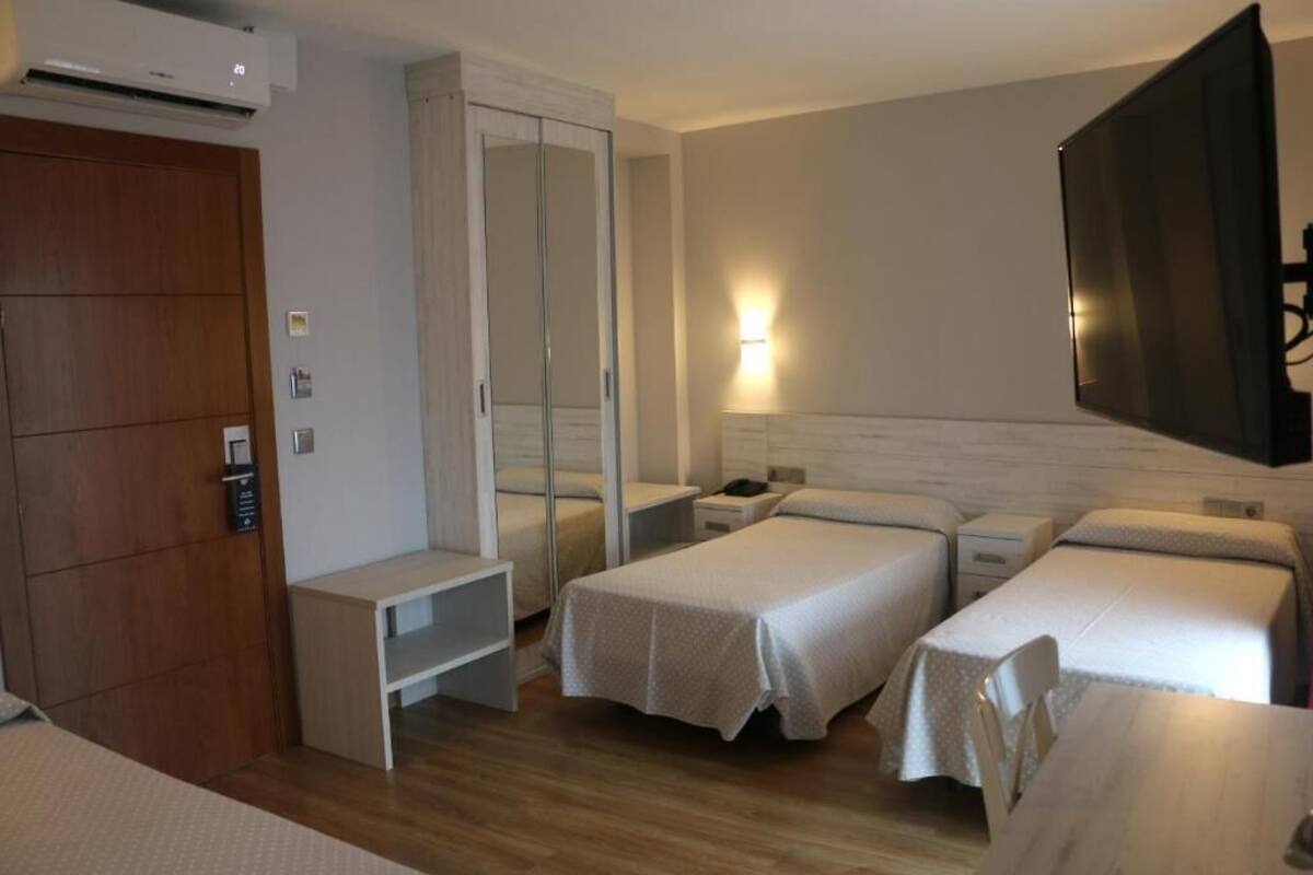 A hotel room with two single beds, a wardrobe, a desk, and a TV mounted on the wall.