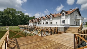 A large white building with a red-tiled roof, connected to a wooden dock over a body of water.