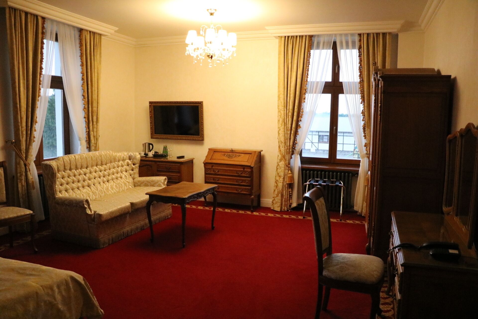 Une chambre d’hôtel avec un tapis rouge, un canapé, une commode en bois, une télévision et une grande fenêtre avec des rideaux.