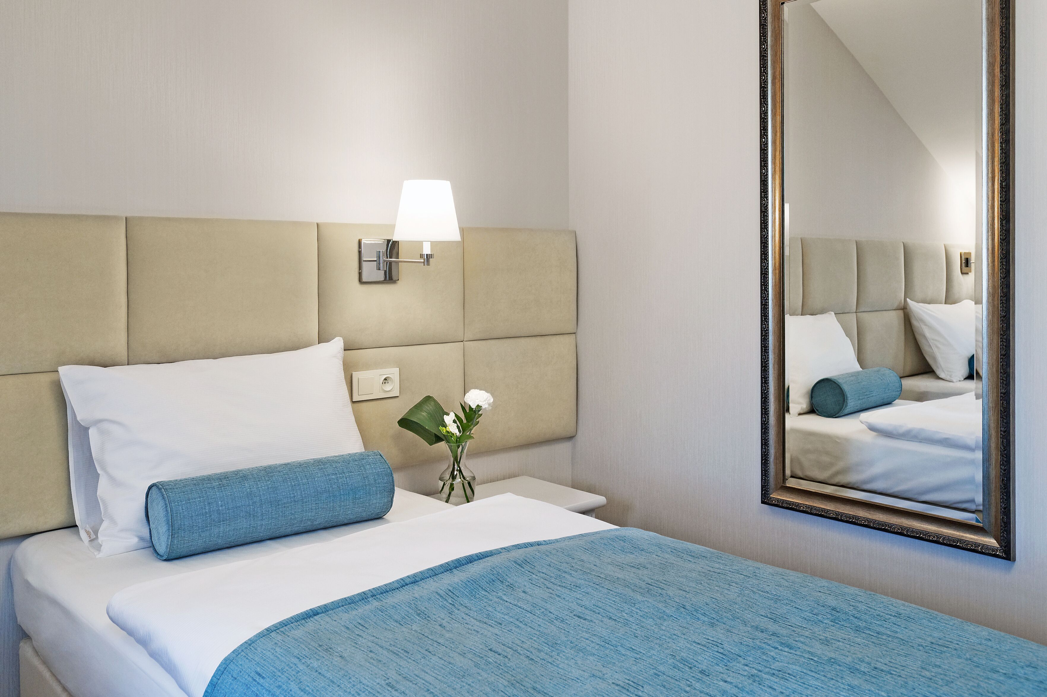 Una habitación de hotel con cama, mesita de noche, lámpara y espejo.