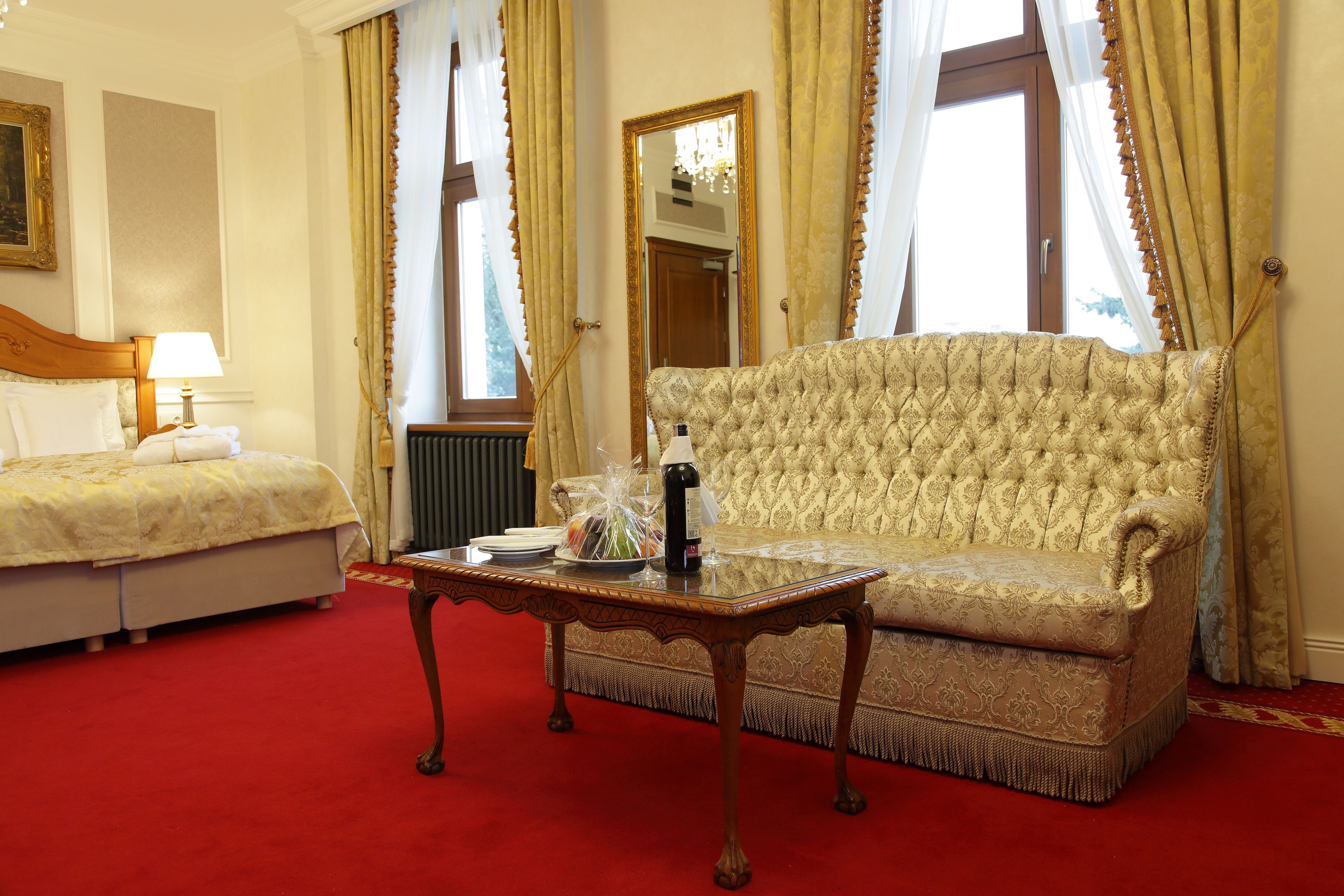 Een hotelkamer met een bed, een bank, een tafel met een fles en gordijnen.